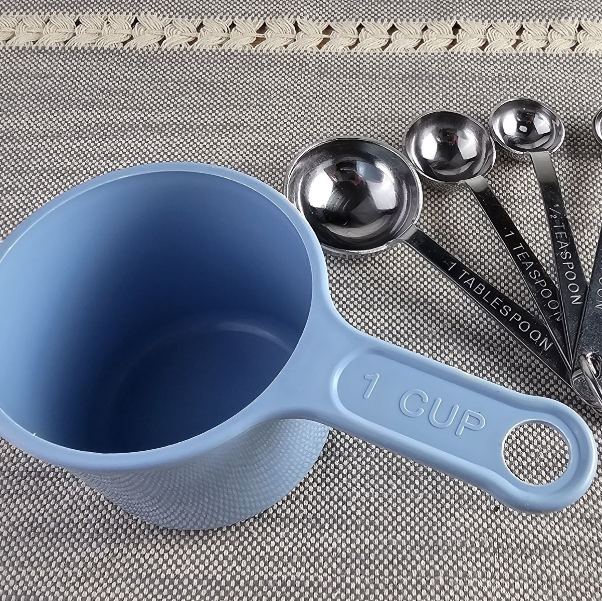 Tablespoons and teaspoons next to a blue cup.